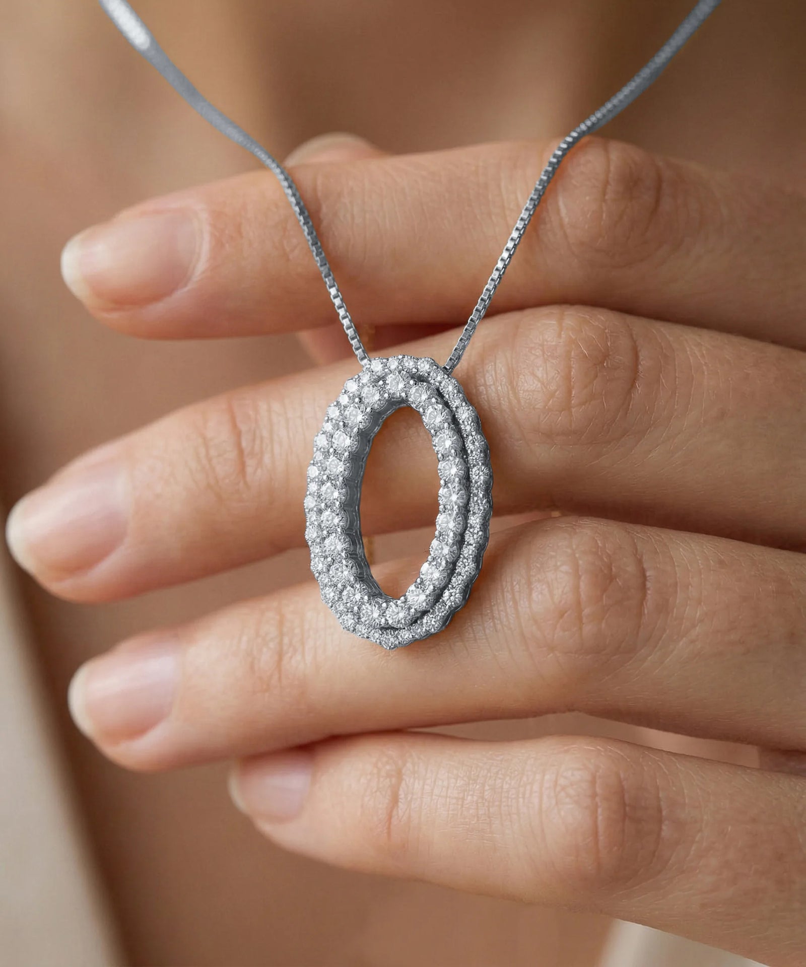 Silver necklace with a pendant held by a hand against a neutral background