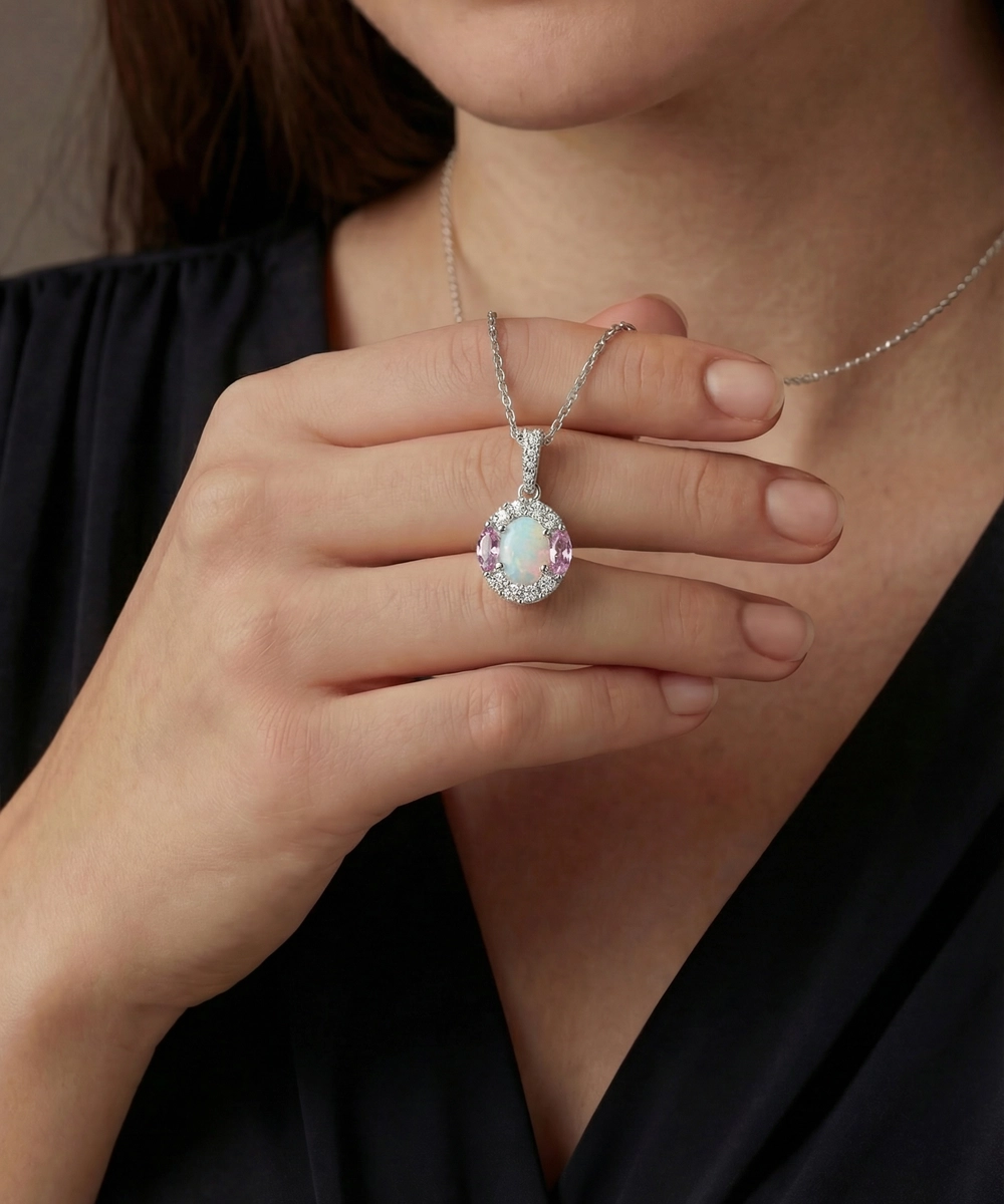 Necklace with a pink gemstone pendant held by a person wearing a black top.