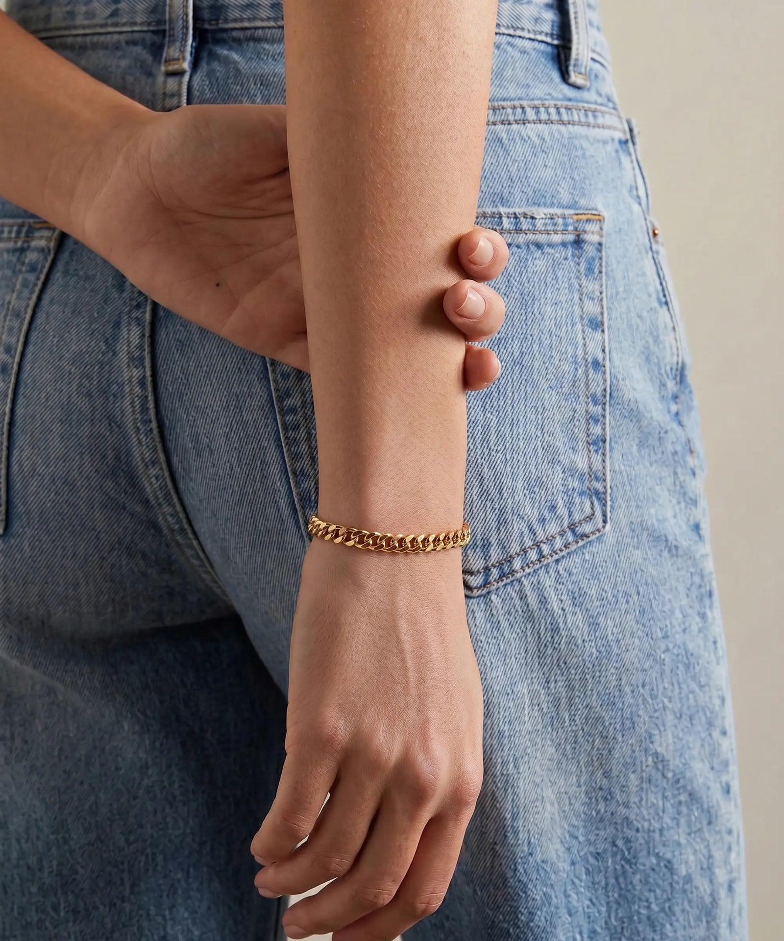 Person wearing a gold bracelet with blue jeans