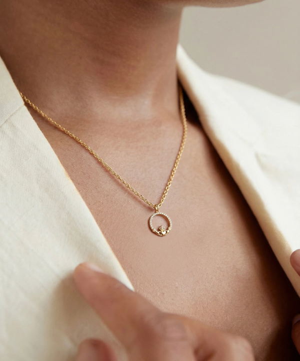 Silver necklace with a circular pendant worn by a person in a beige outfit.