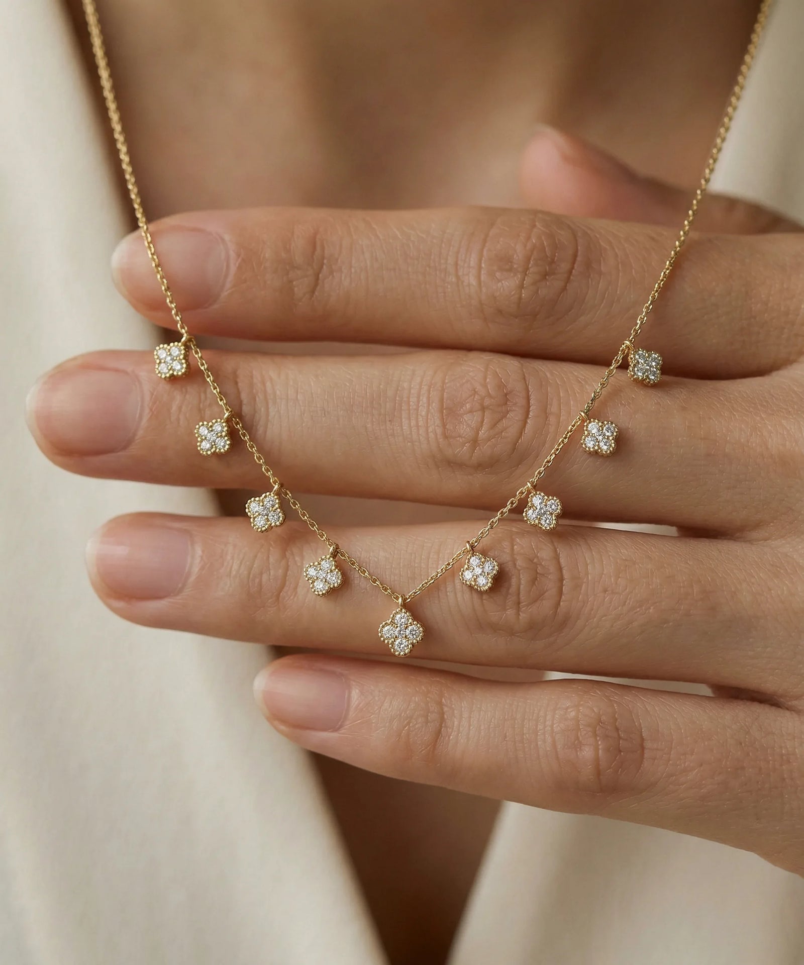 Silver necklace with diamond pendants held by a hand against a neutral background