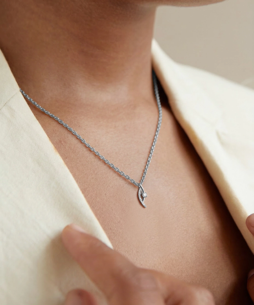 Silver necklace with a delicate pendant worn by a person in a light-colored outfit.