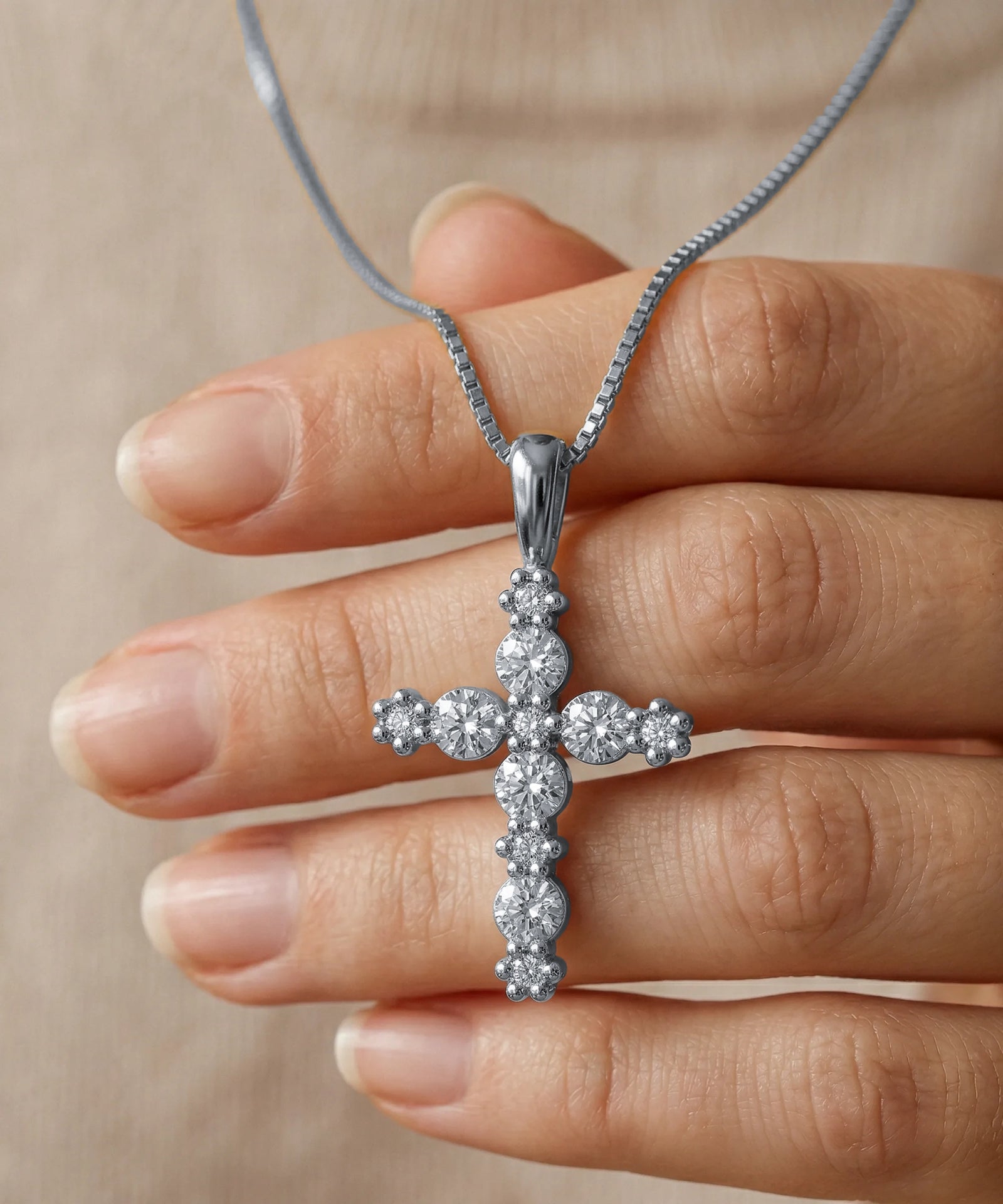 Diamond cross necklace held in a hand against a neutral background
