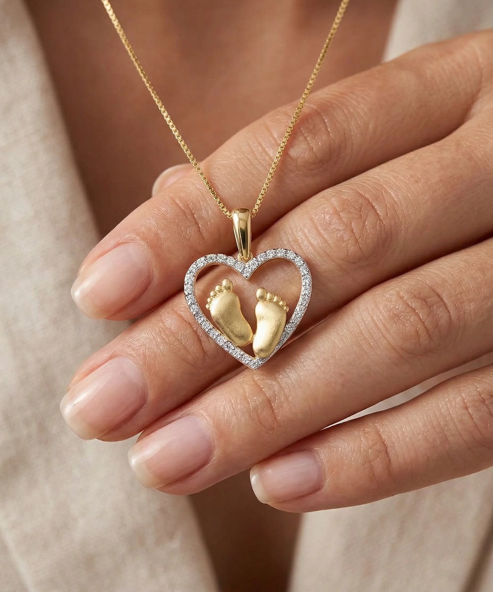 Heart-shaped pendant with gold footprints held by a hand against a neutral background