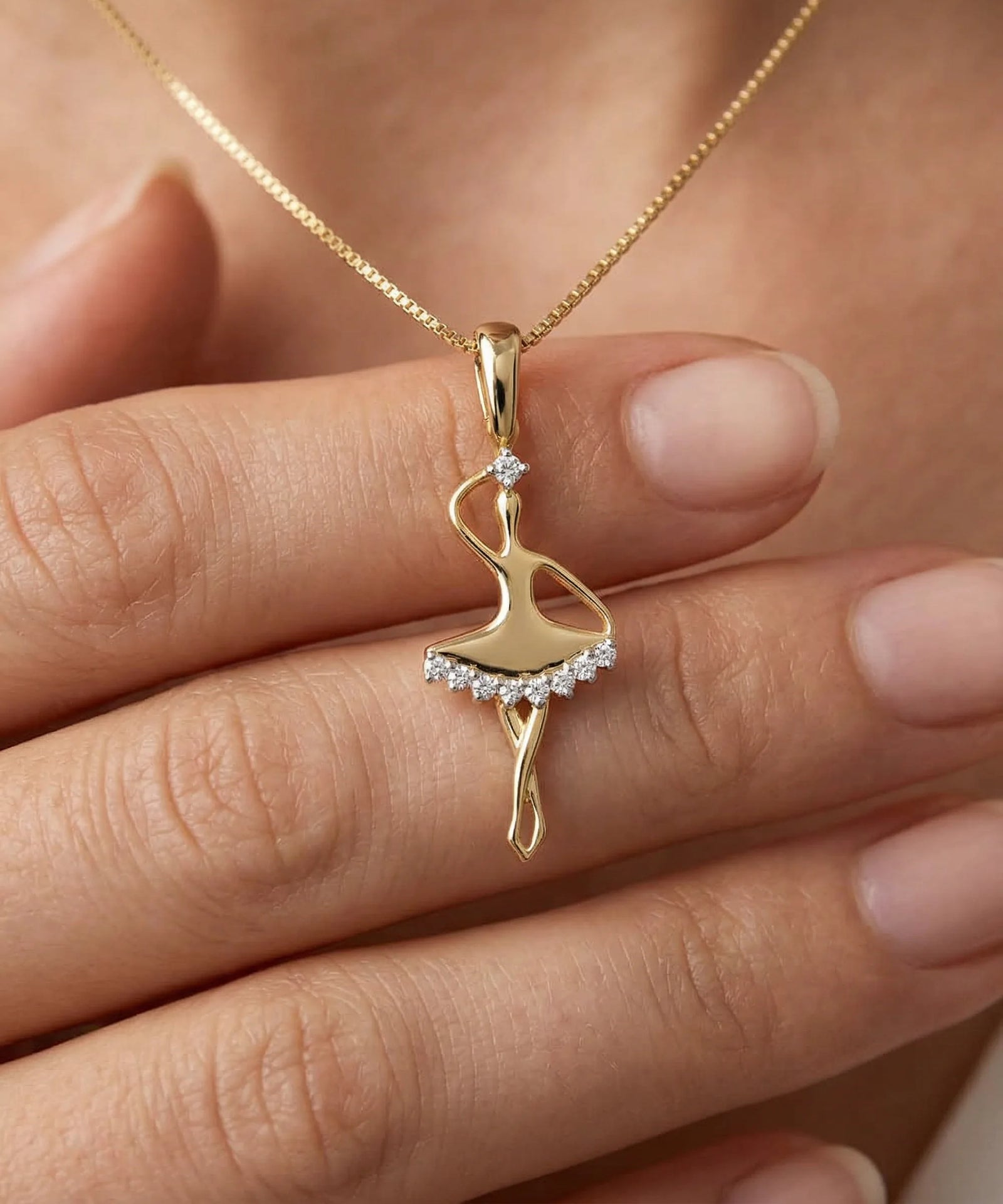 Gold ballerina pendant necklace on a hand