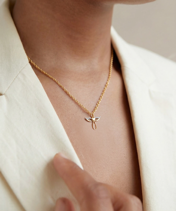 Gold necklace with a delicate pendant worn by a person in a cream blazer.