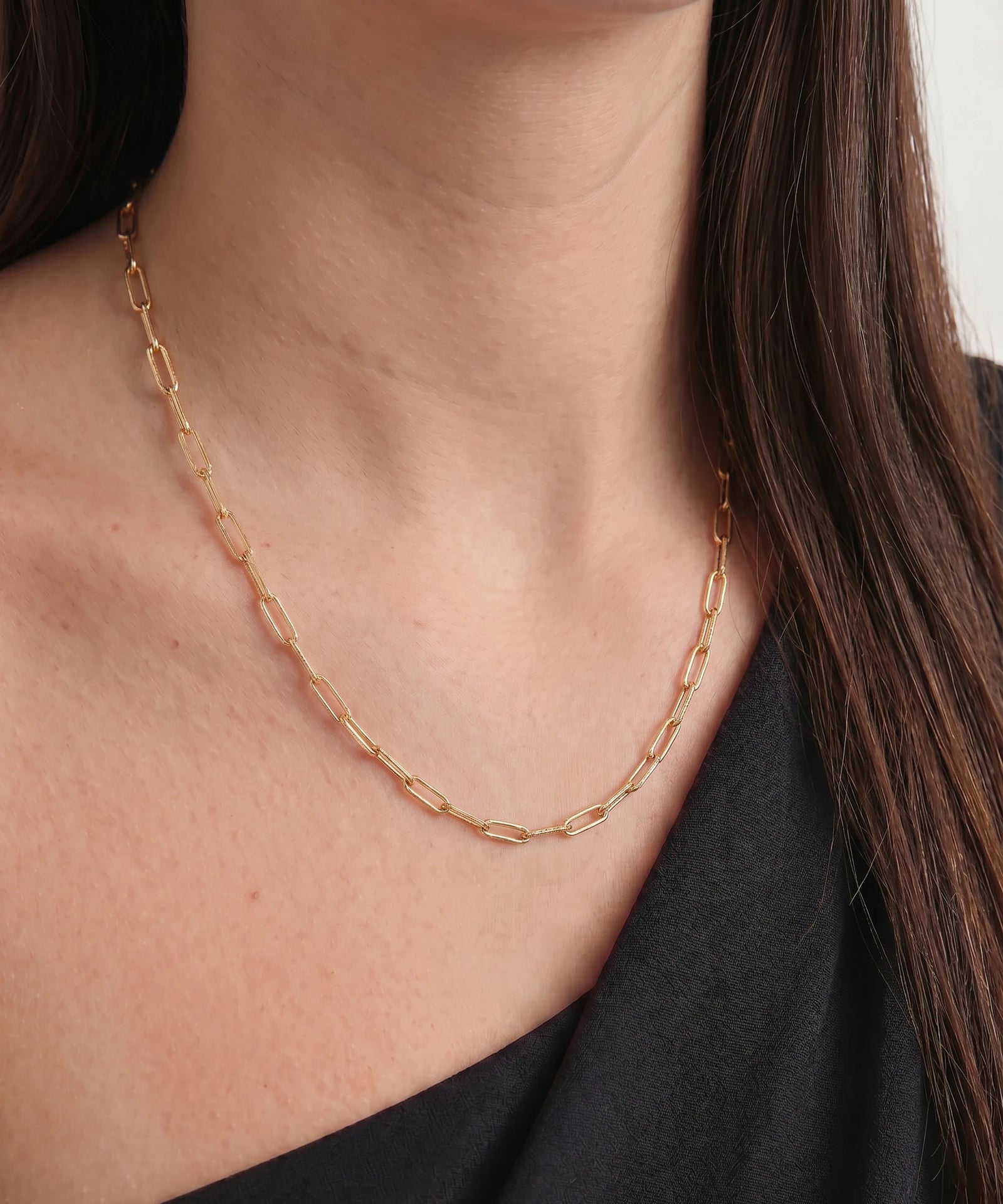 Gold chain necklace worn by a person with a neutral background