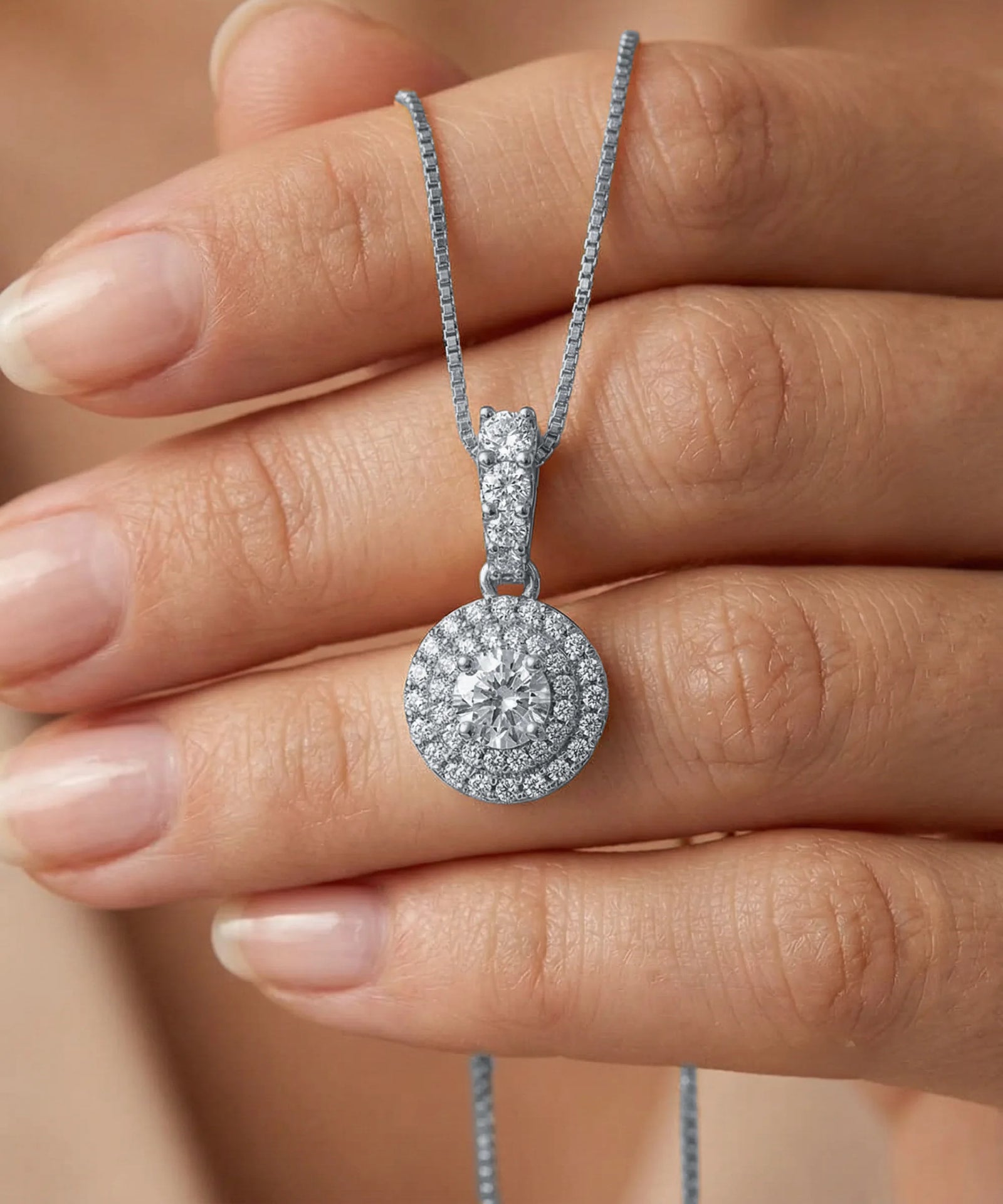 Diamond necklace held between fingers against a neutral background