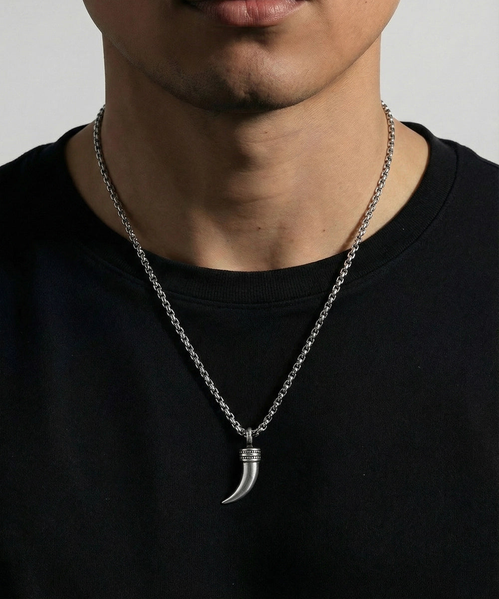 Person wearing a black shirt with a silver necklace featuring a horn pendant against a neutral background