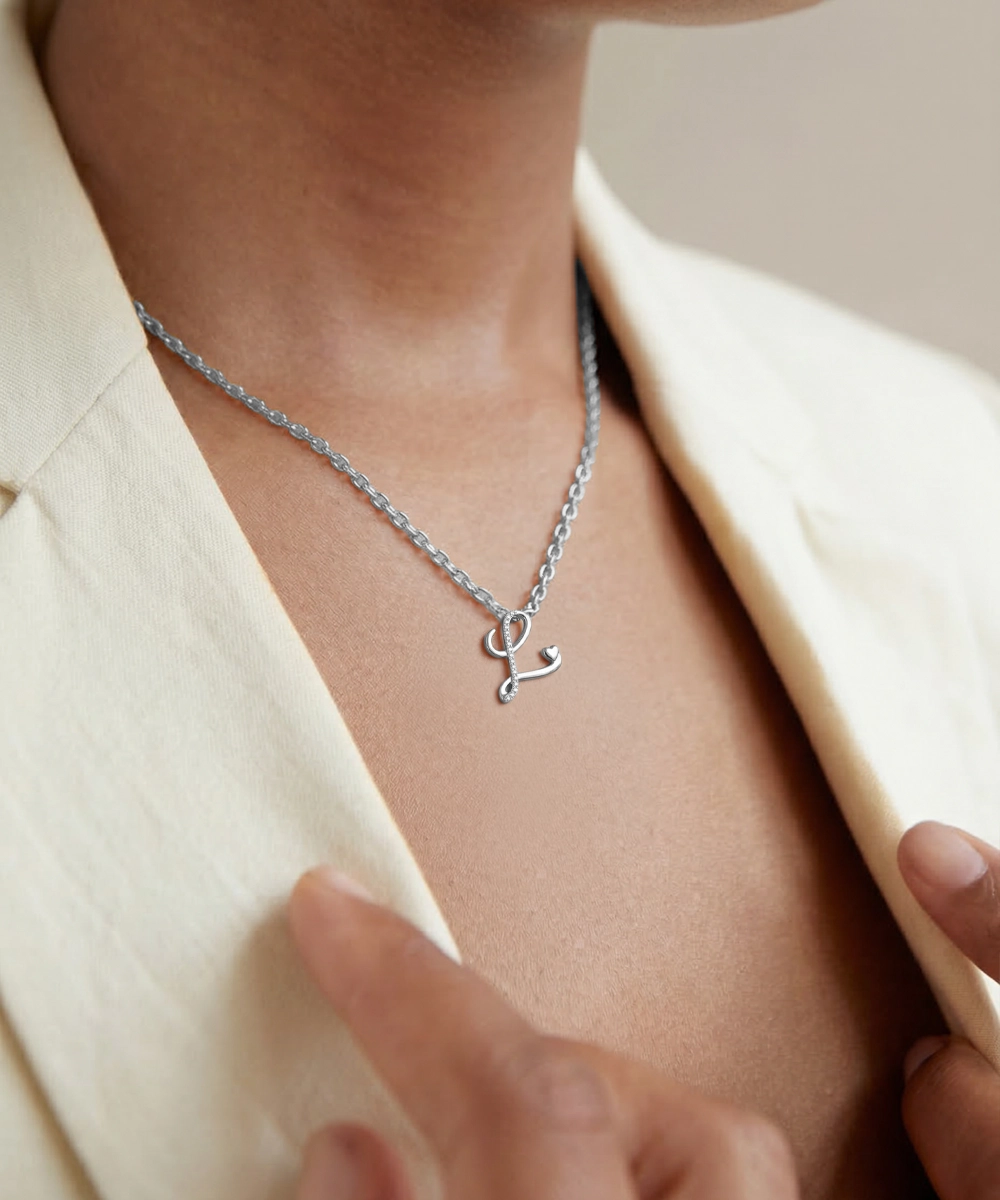 Silver necklace with a unique pendant worn by a person in a beige outfit.