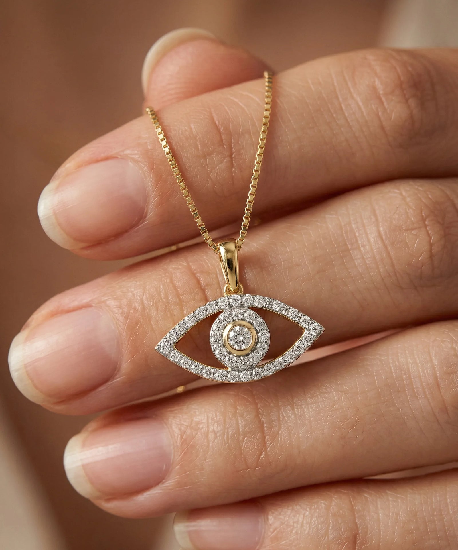 Gold necklace with an eye-shaped pendant held between fingers against a neutral background