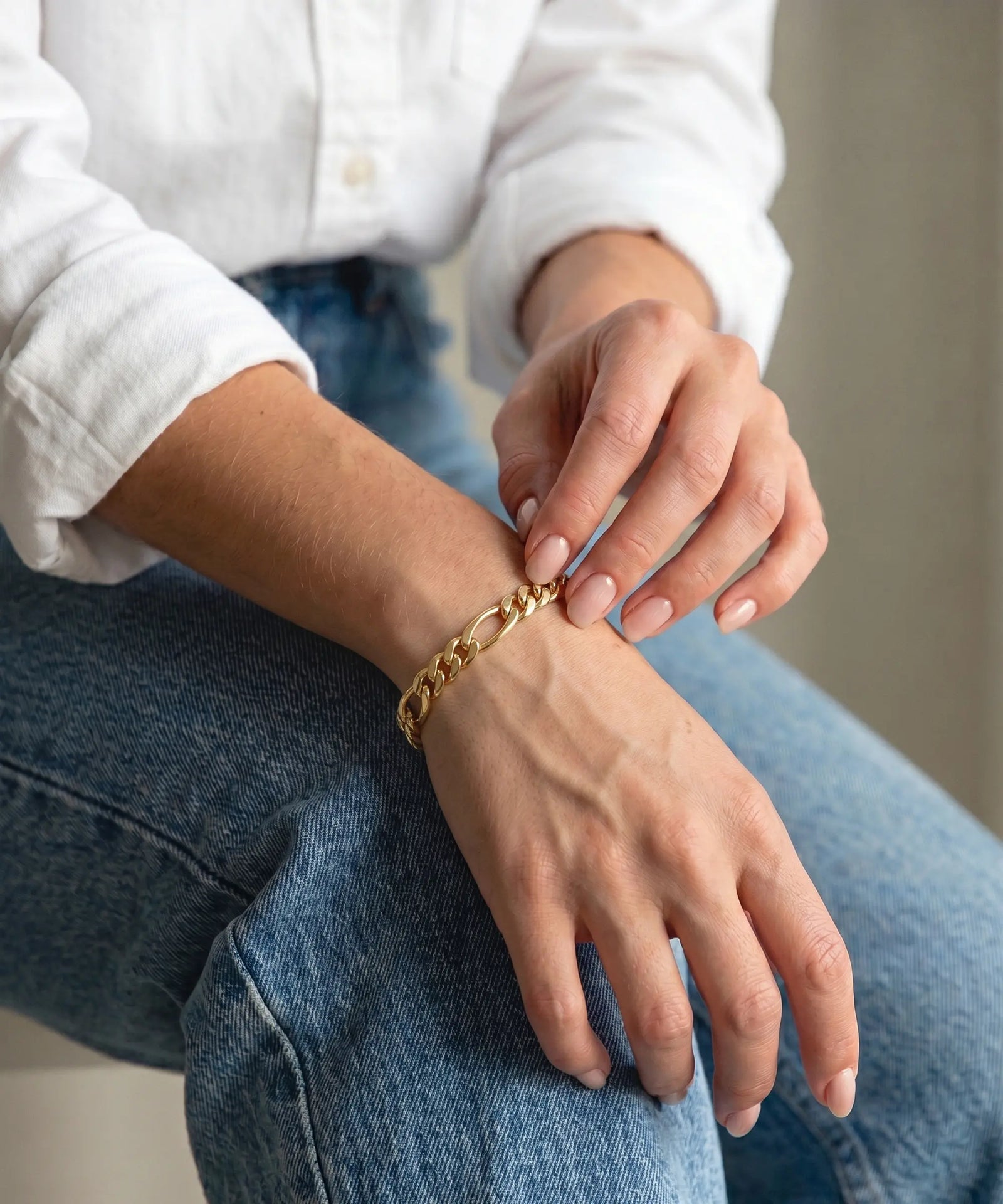 Person wearing gold bracelets on their wrist and hand, sitting on a white surface.