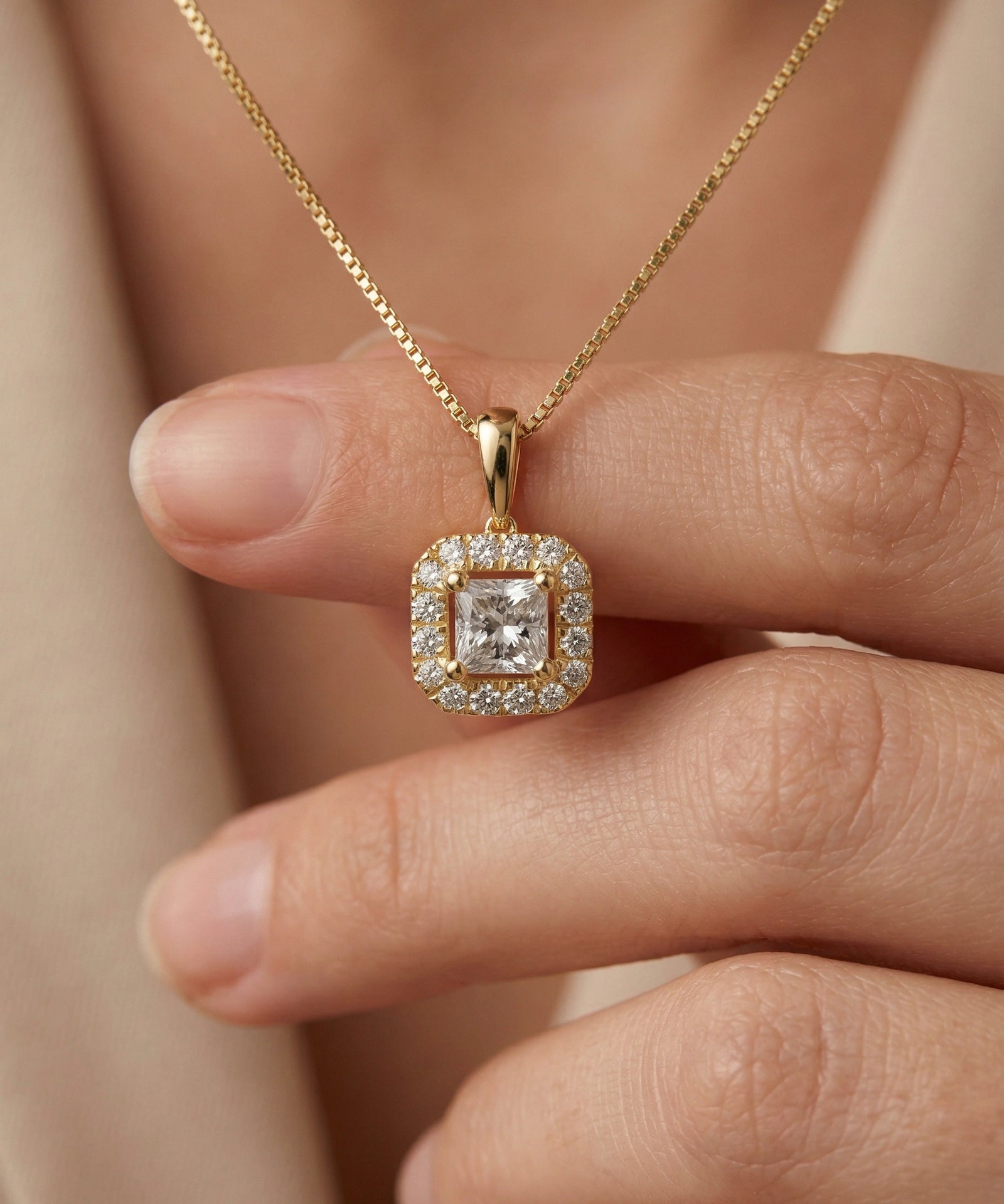 Gold necklace with a diamond pendant held by a hand against a neutral background