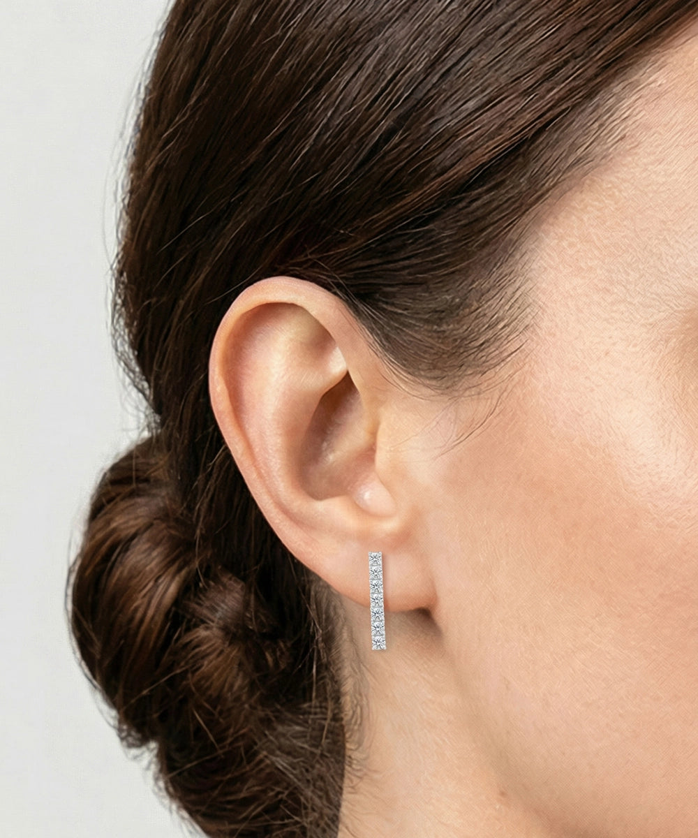 Close-up of an ear wearing a silver hoop earring with a plain background