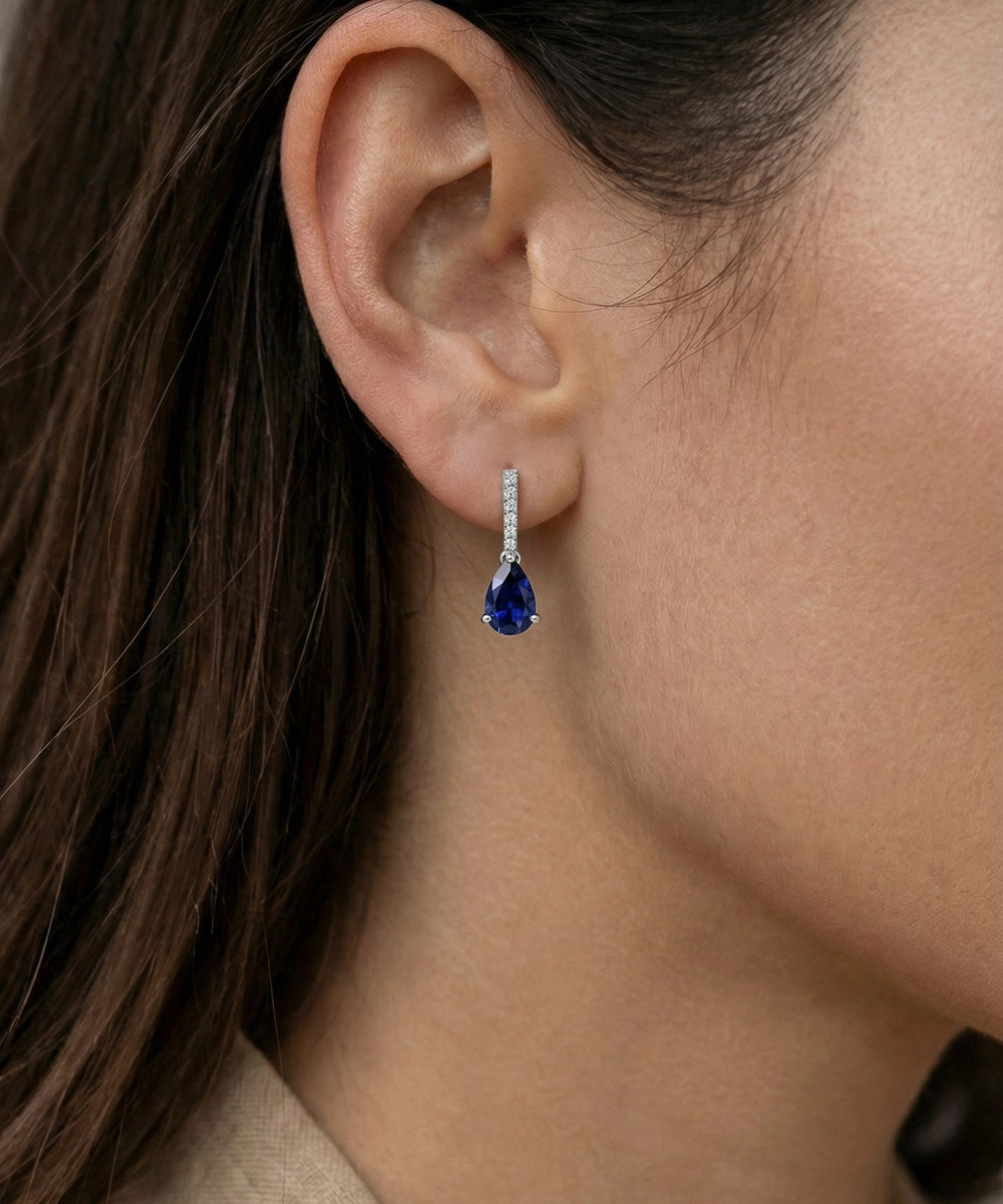 Close-up of an ear wearing a teardrop-shaped blue gemstone earring.