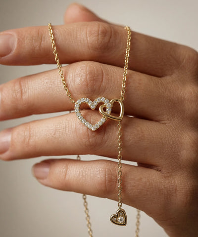 Gold necklace with a heart pendant held by a hand against a neutral background - alternate view