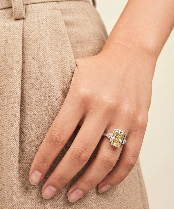Hand wearing a yellow diamond ring with a neutral background