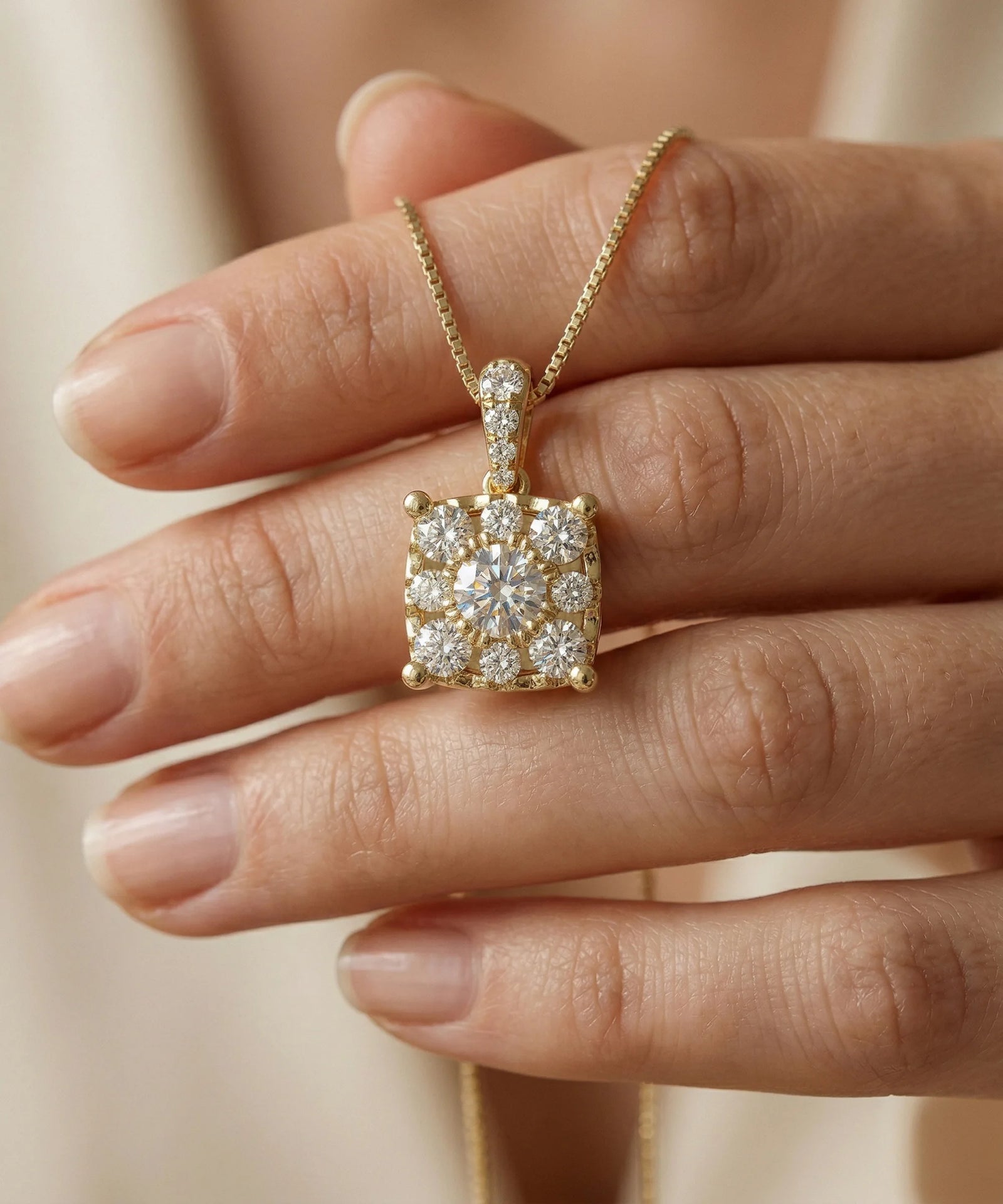 Gold necklace with a diamond pendant held by a hand against a neutral background