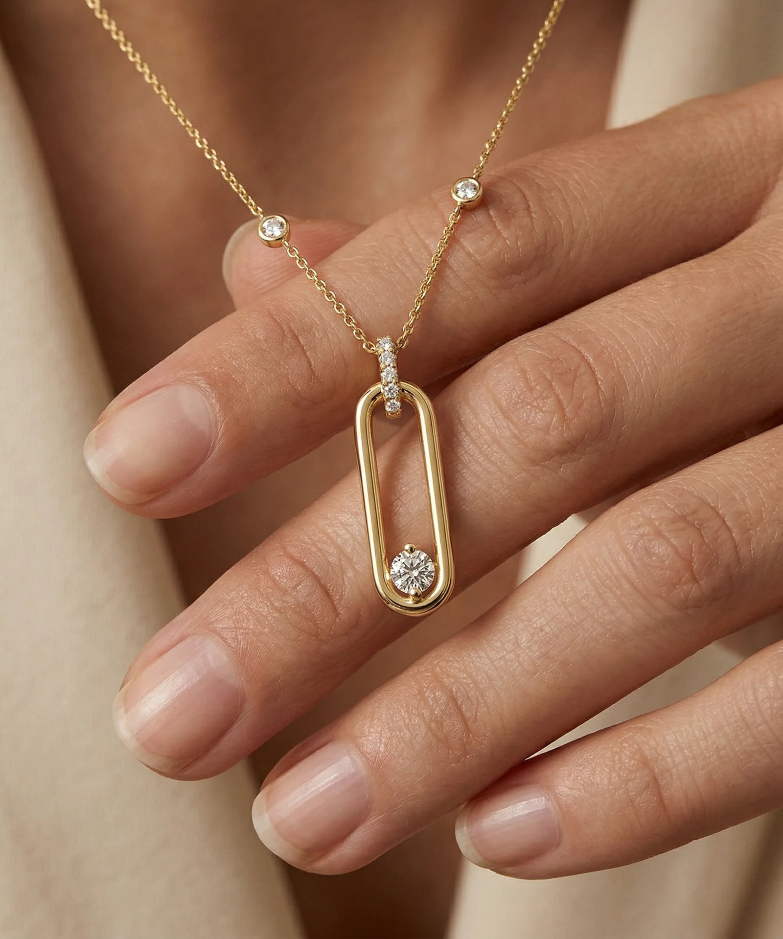 Gold necklace with a diamond pendant on a hand against a neutral background