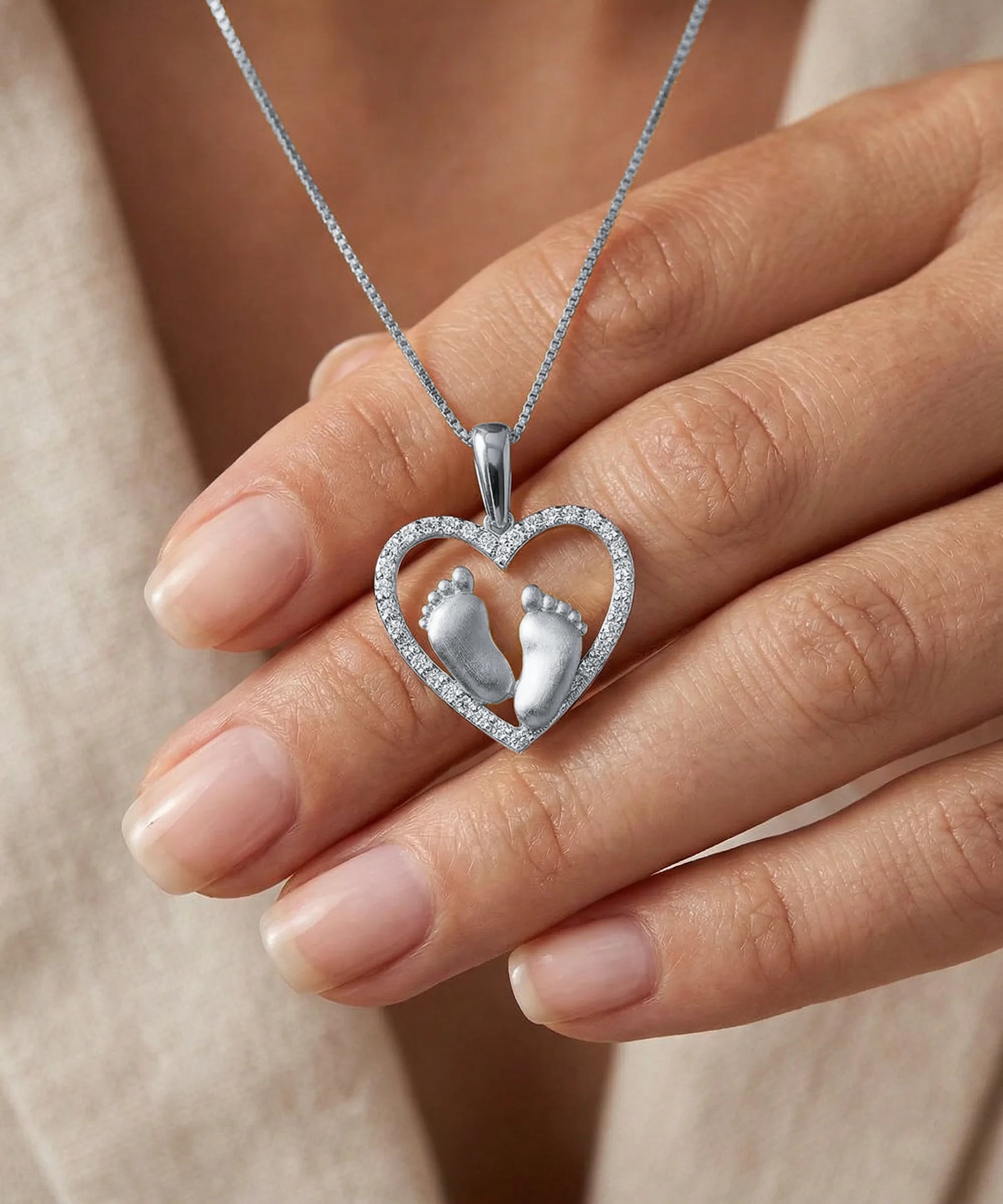 Heart-shaped pendant with footprints held by a hand against a neutral background
