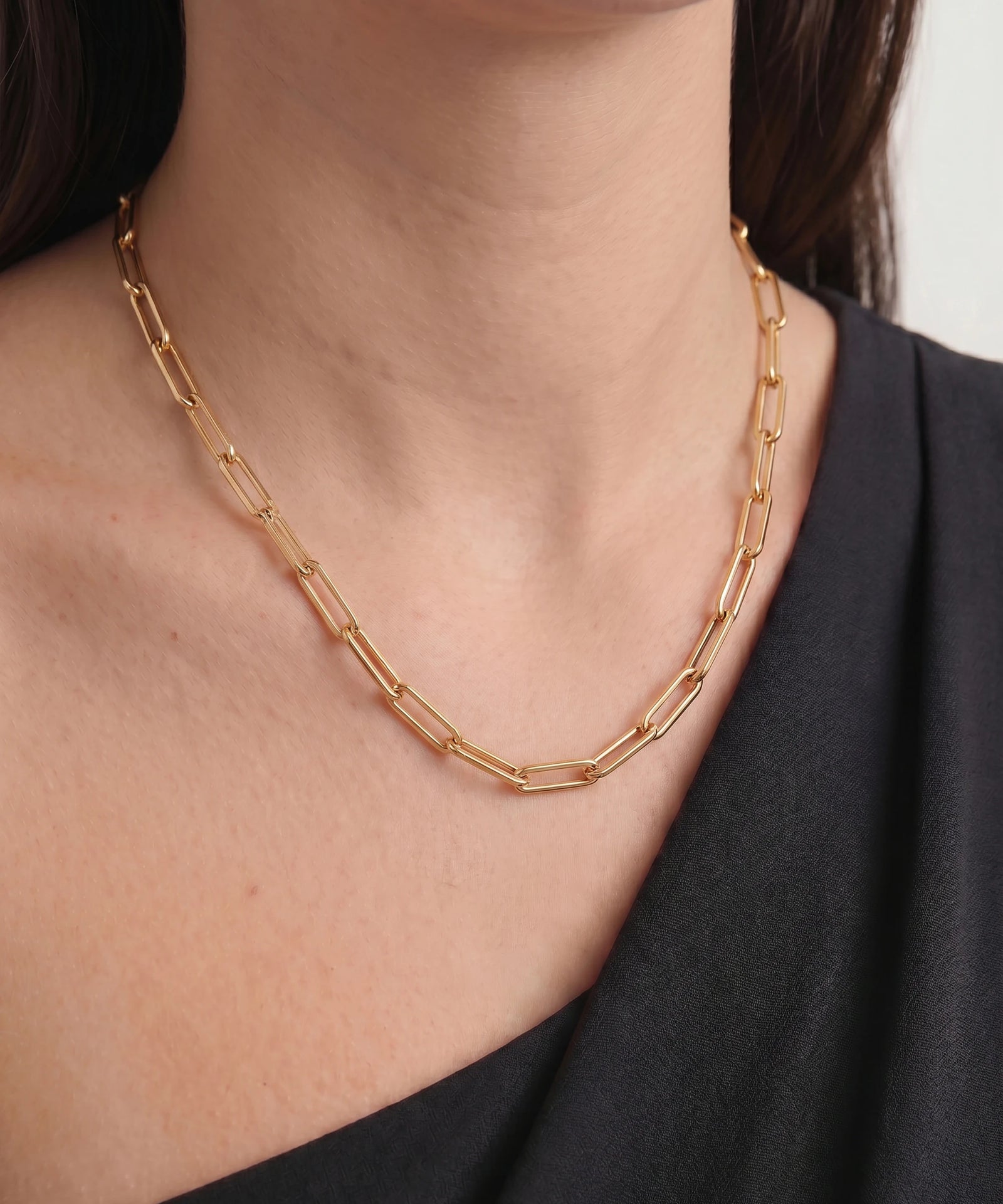 Gold chain necklace worn by a person against a neutral background