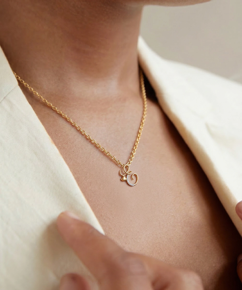 Gold necklace with a small pendant worn by a person in a light-colored outfit.