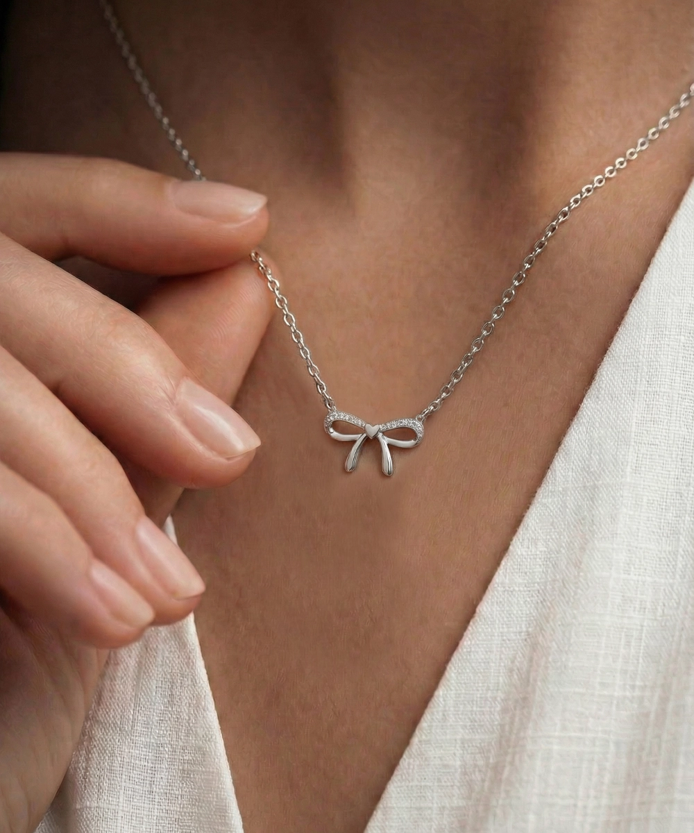 Silver necklace with a leaf pendant worn by a person in a white outfit.
