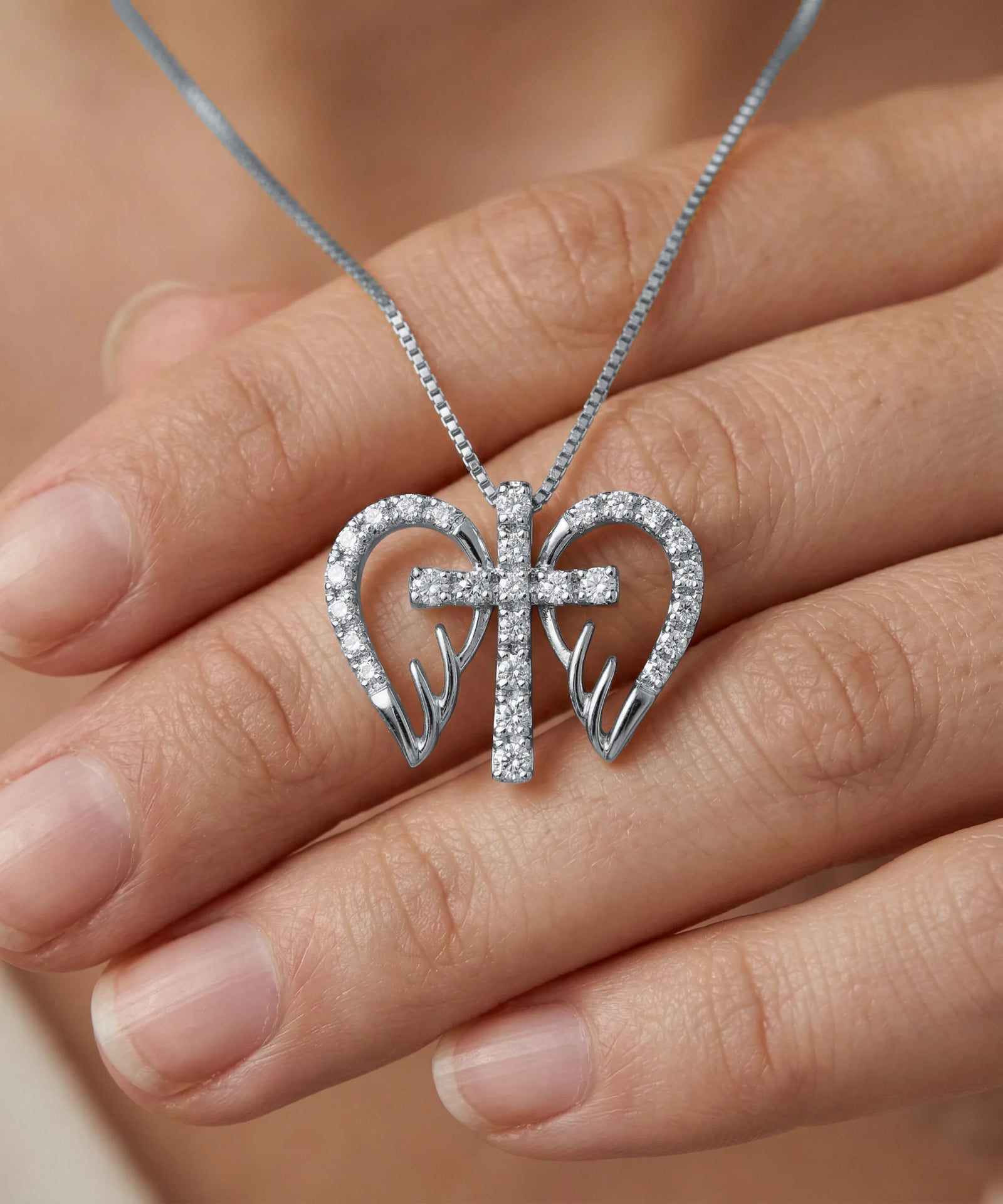 Silver necklace with a heart and cross pendant held in a hand.