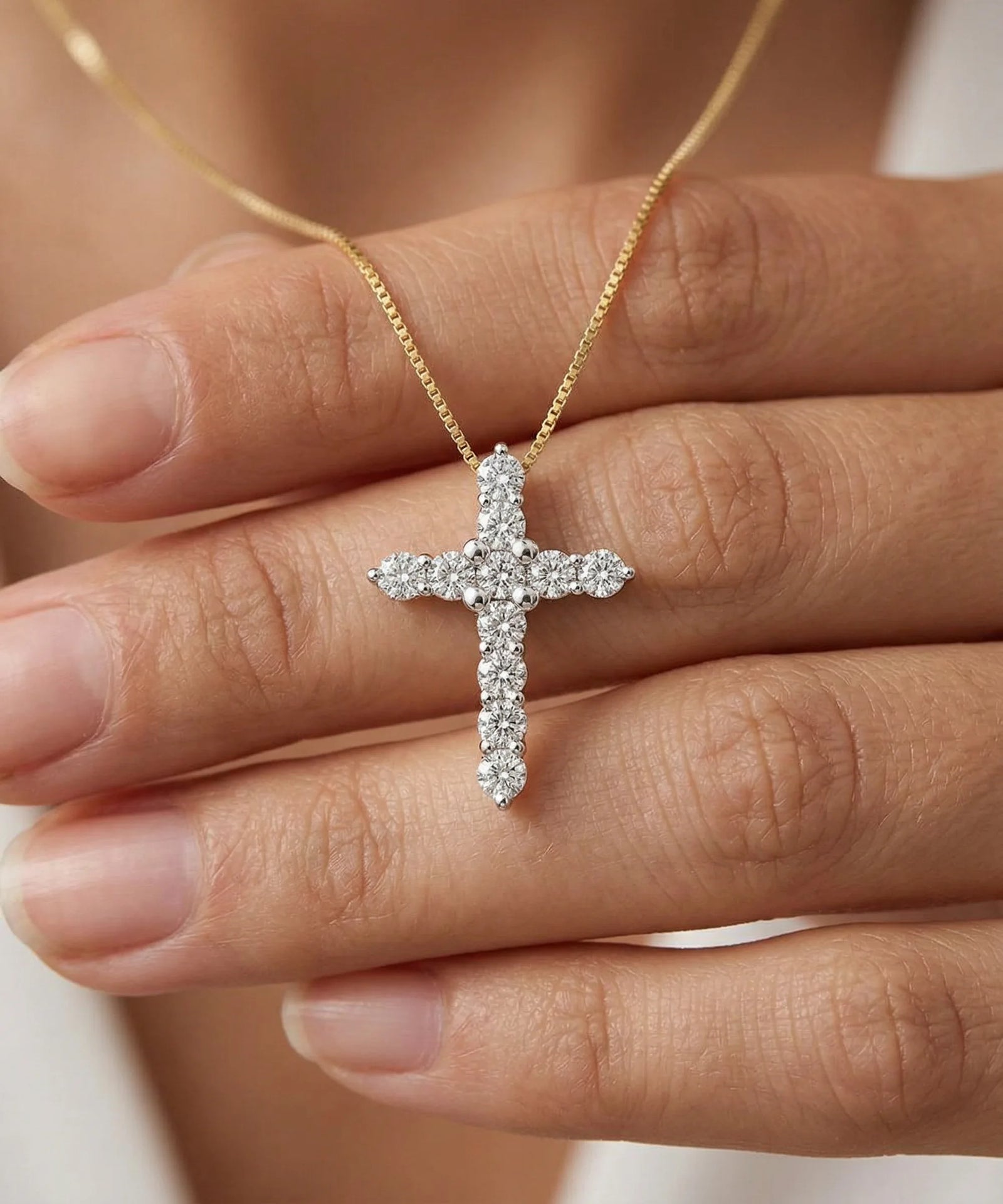 Diamond cross necklace held between fingers against a neutral background