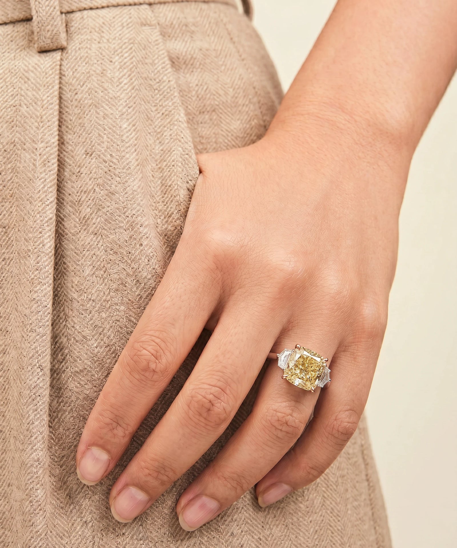 Close-up of a hand wearing a diamond ring on a neutral background