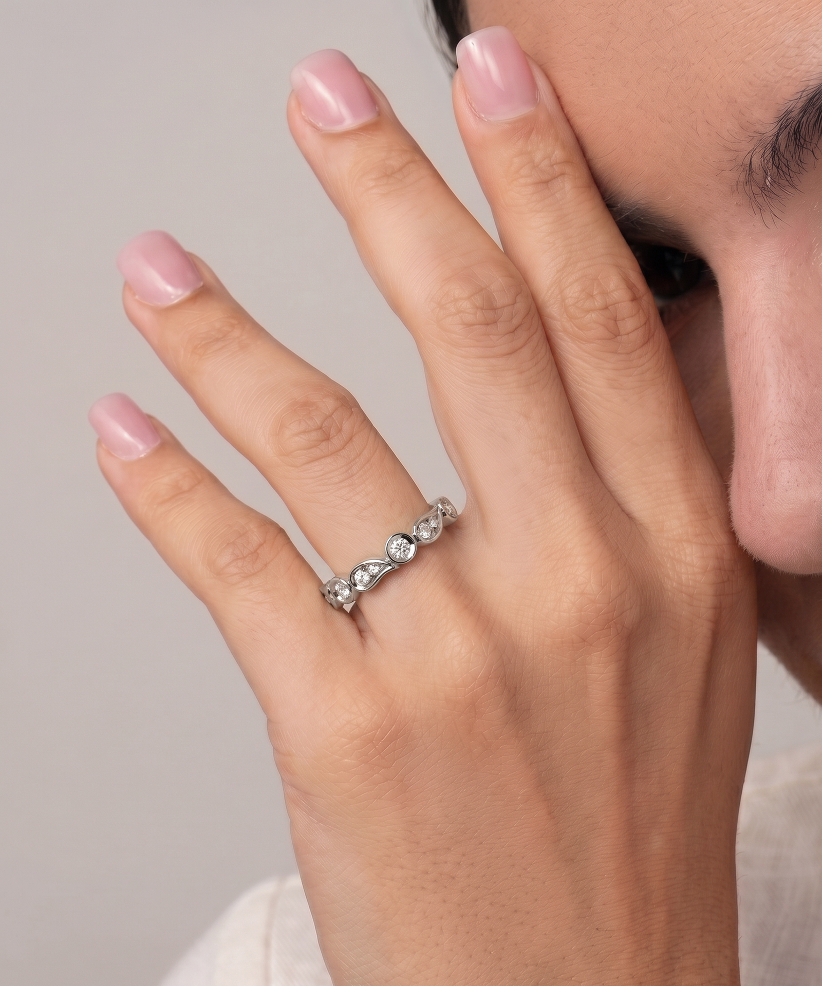 A close-up of a person's hand wearing a silver-toned diamond eternity ring, with their face partially visible in the background.