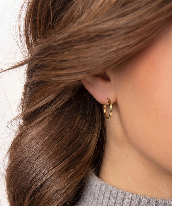 Close-up of an ear wearing a gold hoop earring with brown hair.