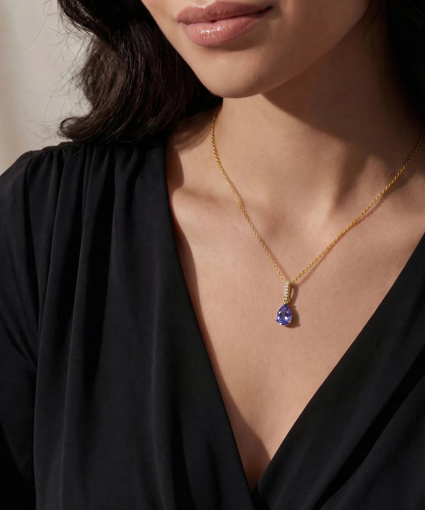 Gold necklace with a blue gemstone pendant worn by a person