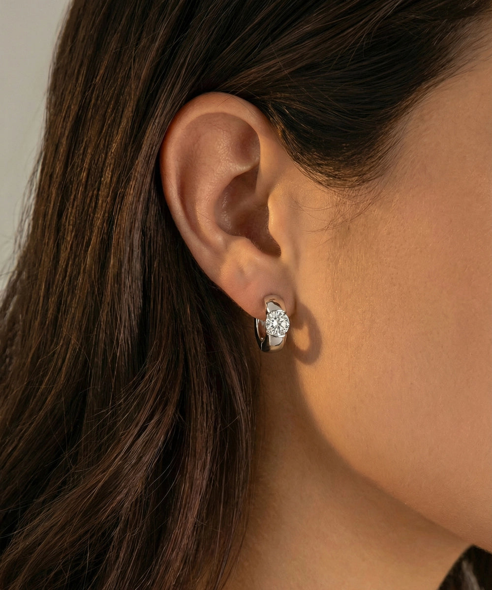 Close-up of an ear wearing a diamond earring with a neutral background