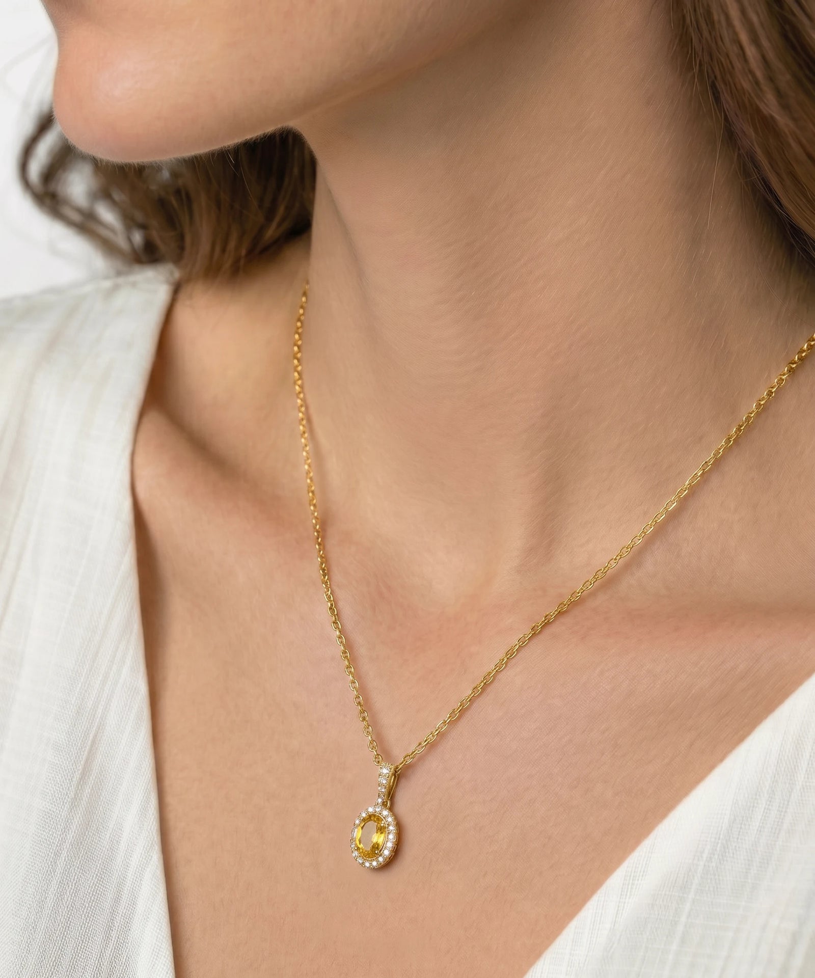 Gold necklace with a yellow gemstone pendant on a person wearing a white top.