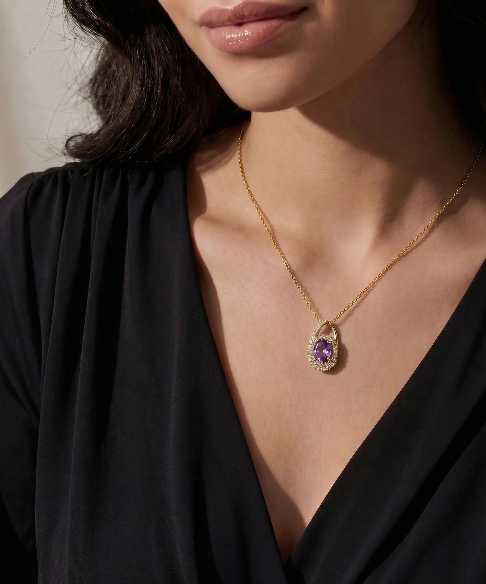 Gold necklace with a green gemstone pendant worn by a person in a black top.