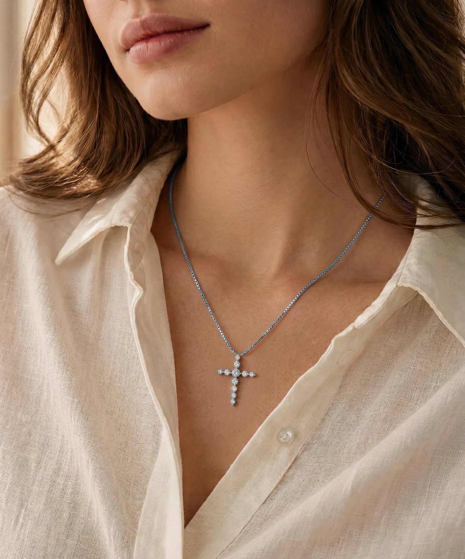 Close-up of a person wearing a silver cross necklace with a beige shirt.