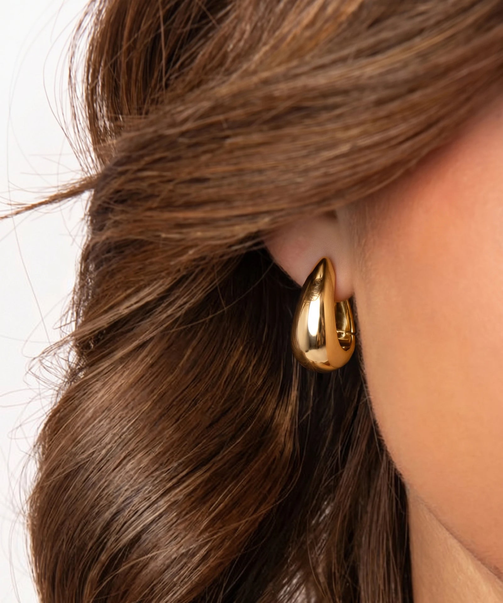 Gold hoop earring worn by a person with brown hair.