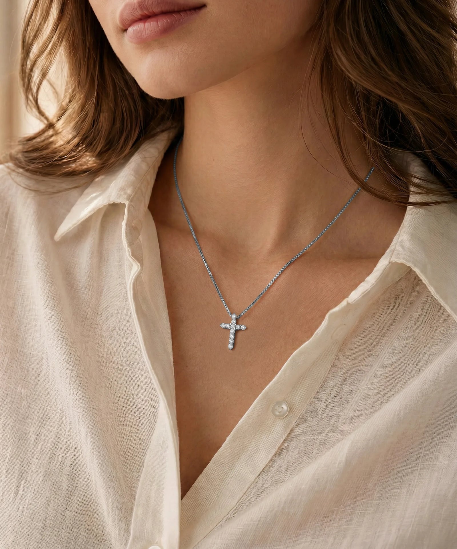 Necklace with a cross pendant worn by a person in a light-colored shirt.