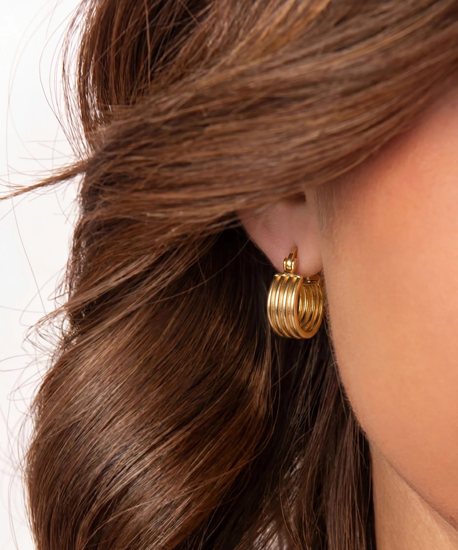 Close-up of a person wearing gold hoop earrings with hair partially covering the face.