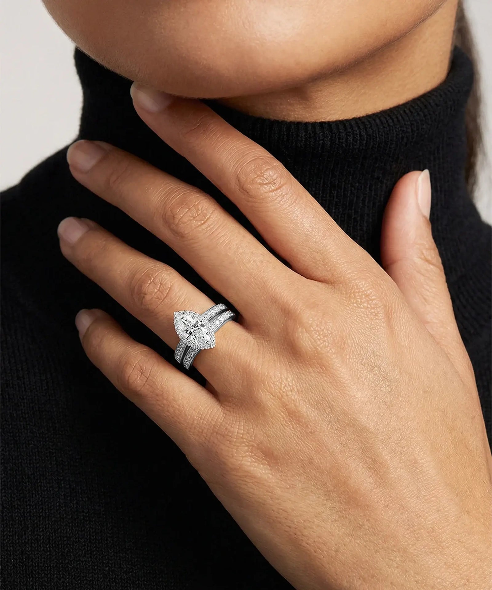 Close-up of a hand wearing a diamond ring with a black turtleneck sweater.