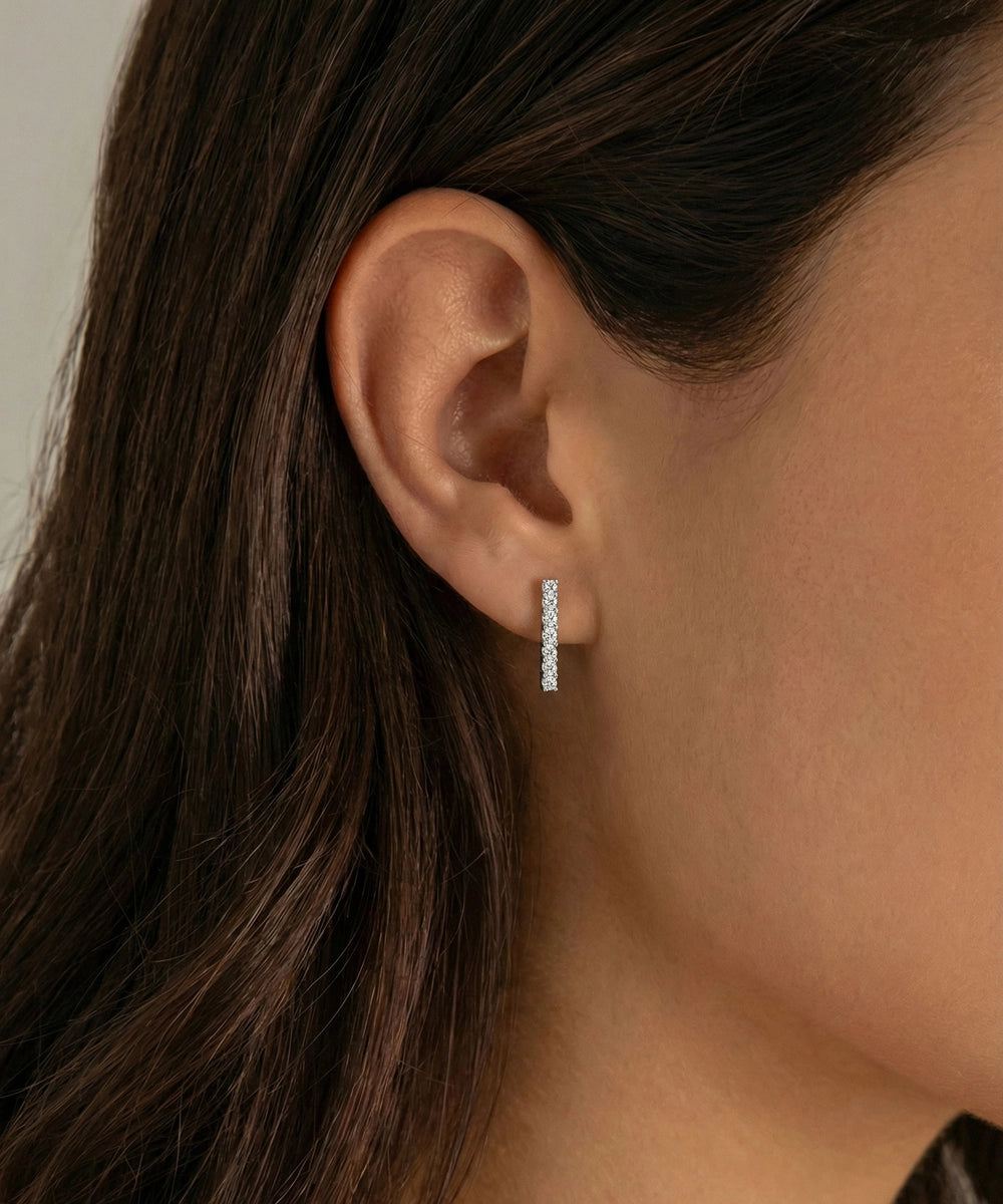Close-up of an ear wearing a diamond hoop earring with dark hair and neutral background