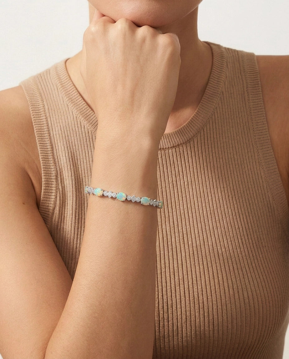 A close-up of a model wearing a delicate bracelet with light blue and white stones on a silver-toned band, paired with a ribbed beige tank top.