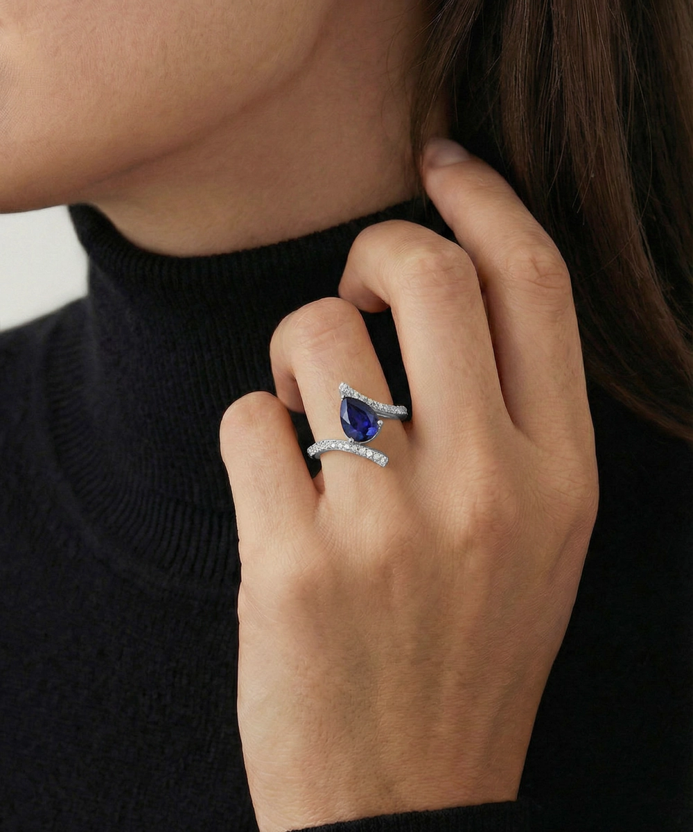 Close-up of a hand wearing a ring with a blue gemstone and black turtleneck sweater.