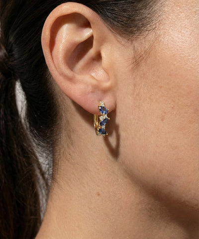 Close-up of an ear wearing a gold earring with blue gemstones. - alternate view