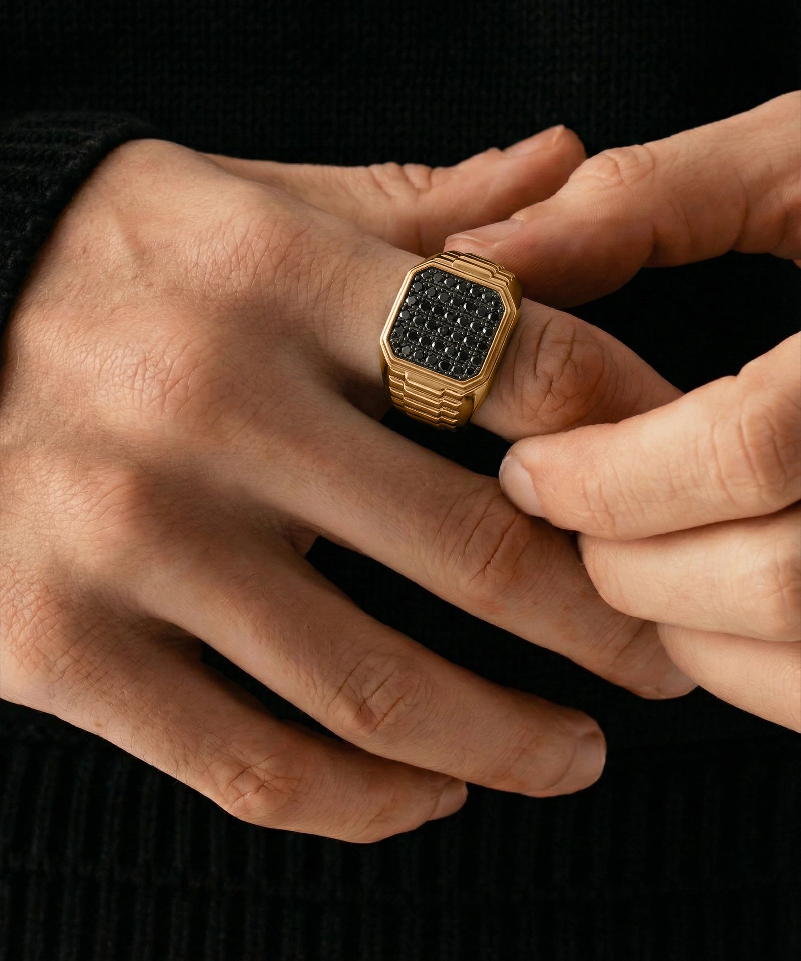 Gold ring with black gemstones on a person's finger against a black background