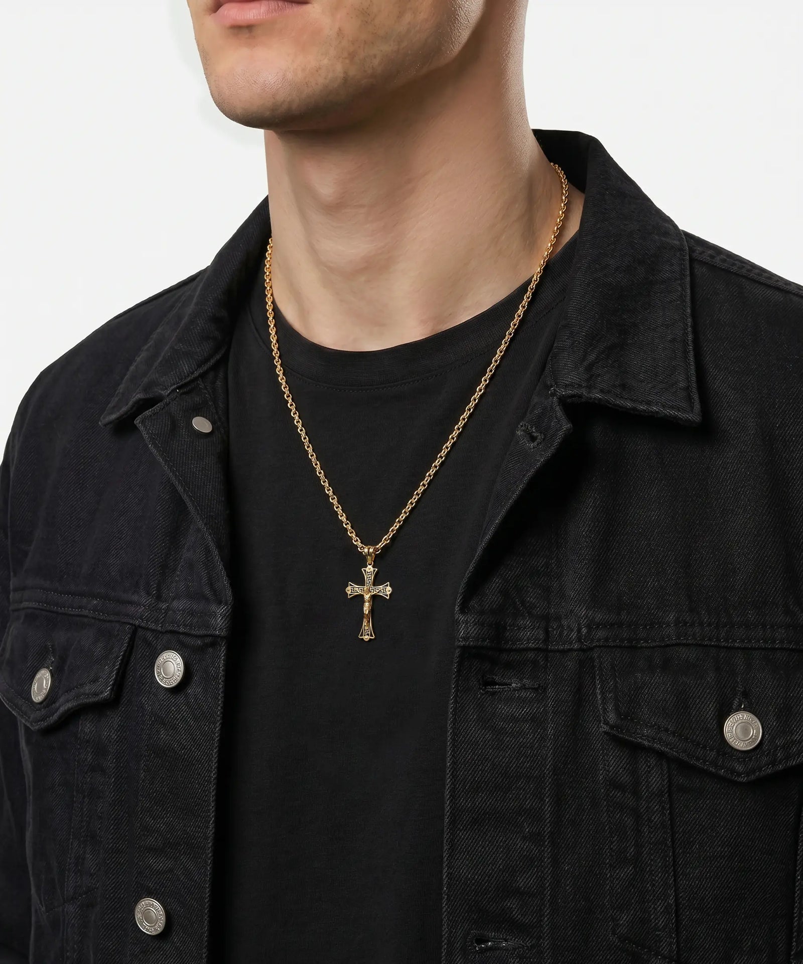 Man wearing a gold necklace with a cross pendant against a plain background