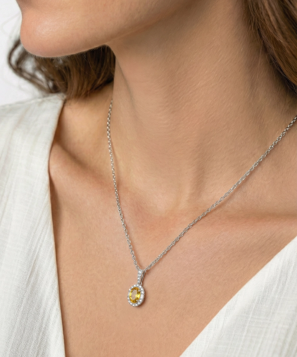 Necklace with a yellow gemstone pendant worn by a person in a white top.