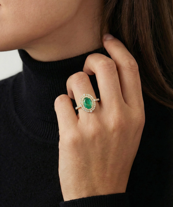 Close-up of a hand wearing an emerald ring with a blurred background
