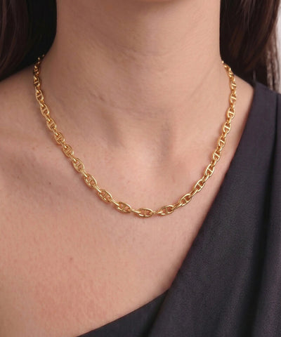 A close-up of a model's neck and upper chest wearing a polished gold chain necklace with interlocking oval links, paired with a dark gray off-the-shoulder top. - alternate view